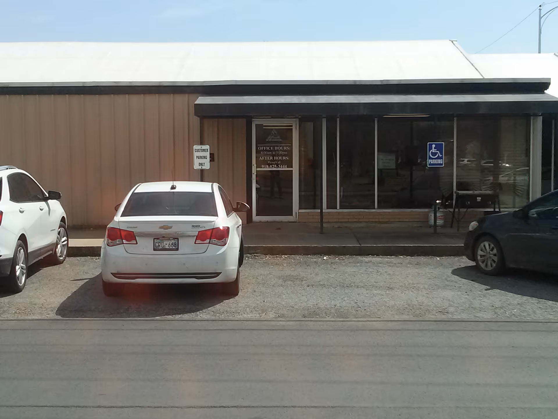 Exterior of a single-story building with glass front entrance and parked cars in front.
