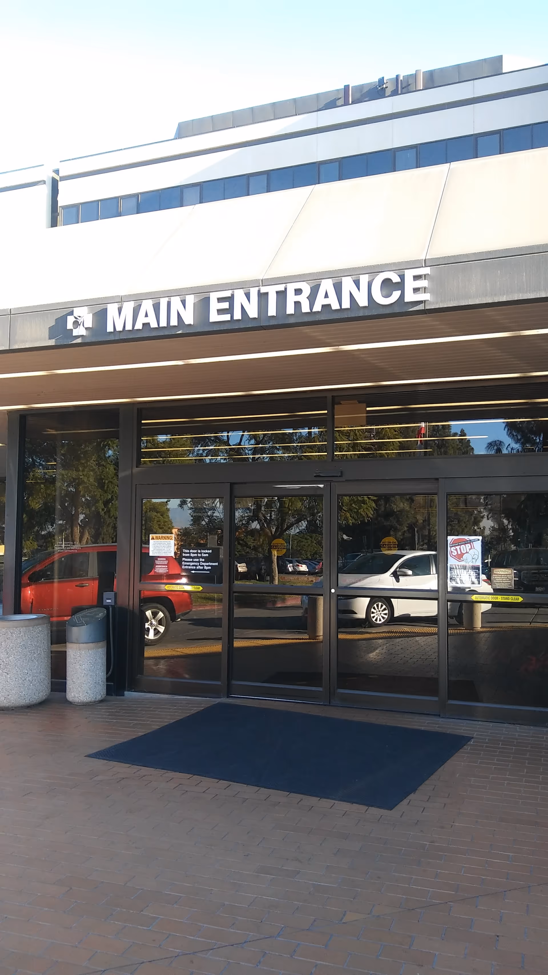 Main entrance of a modern hospital with glass doors and reflections.