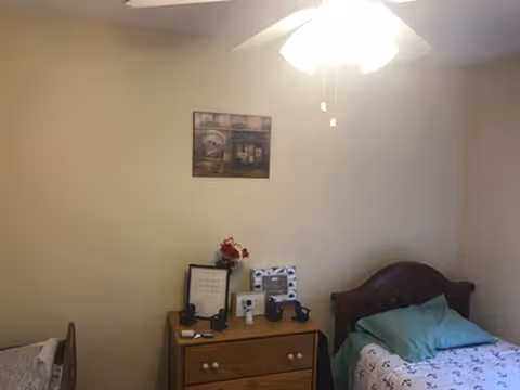 A cozy bedroom in a senior living facility with a wooden bed, nightstand, and decor.