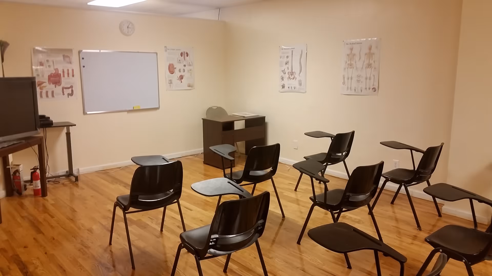 Empty classroom with black plastic chairs, a whiteboard, posters, and a TV.