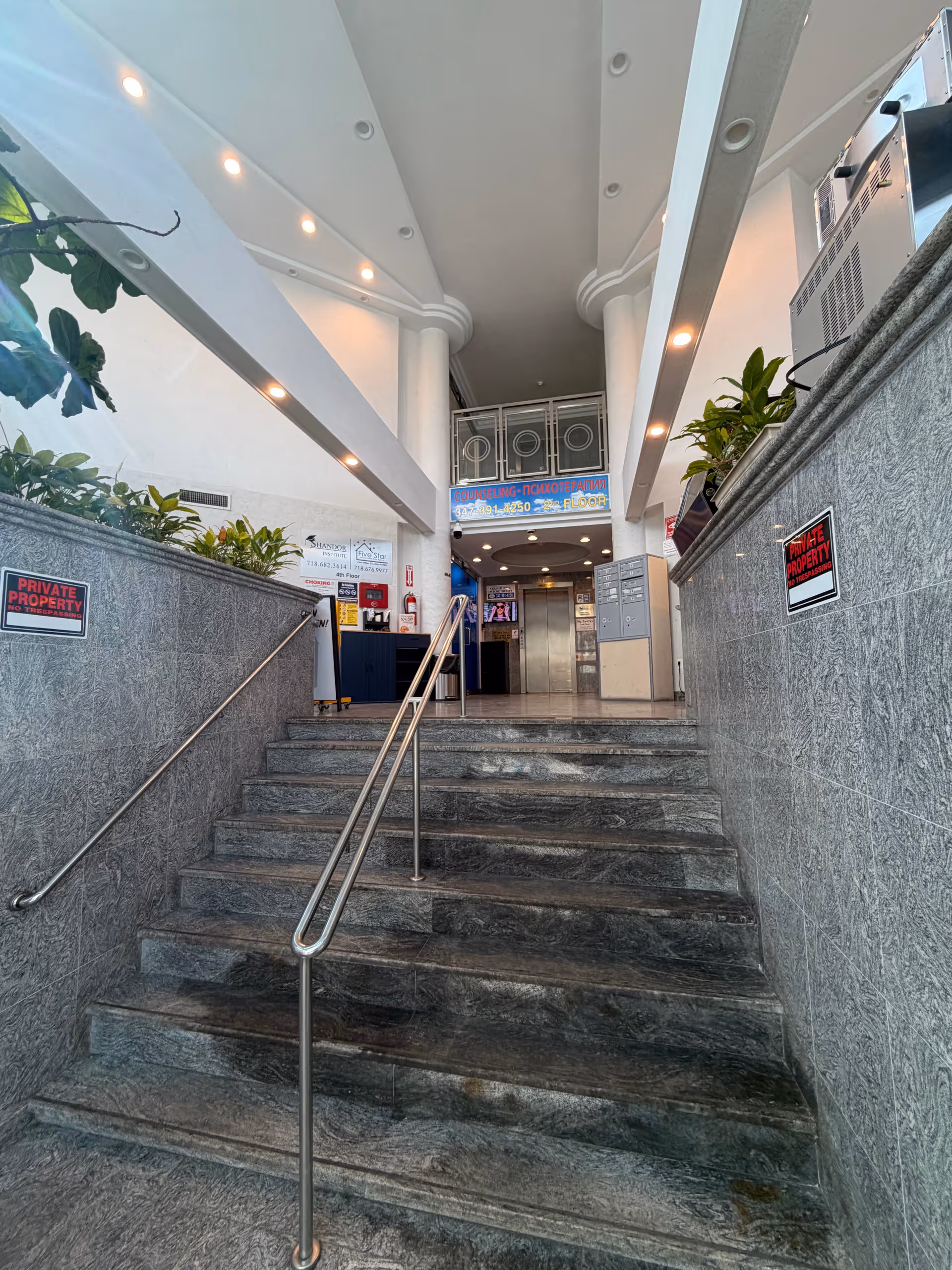 Interior stairwell and entrance area with marble steps, railings, and signs.