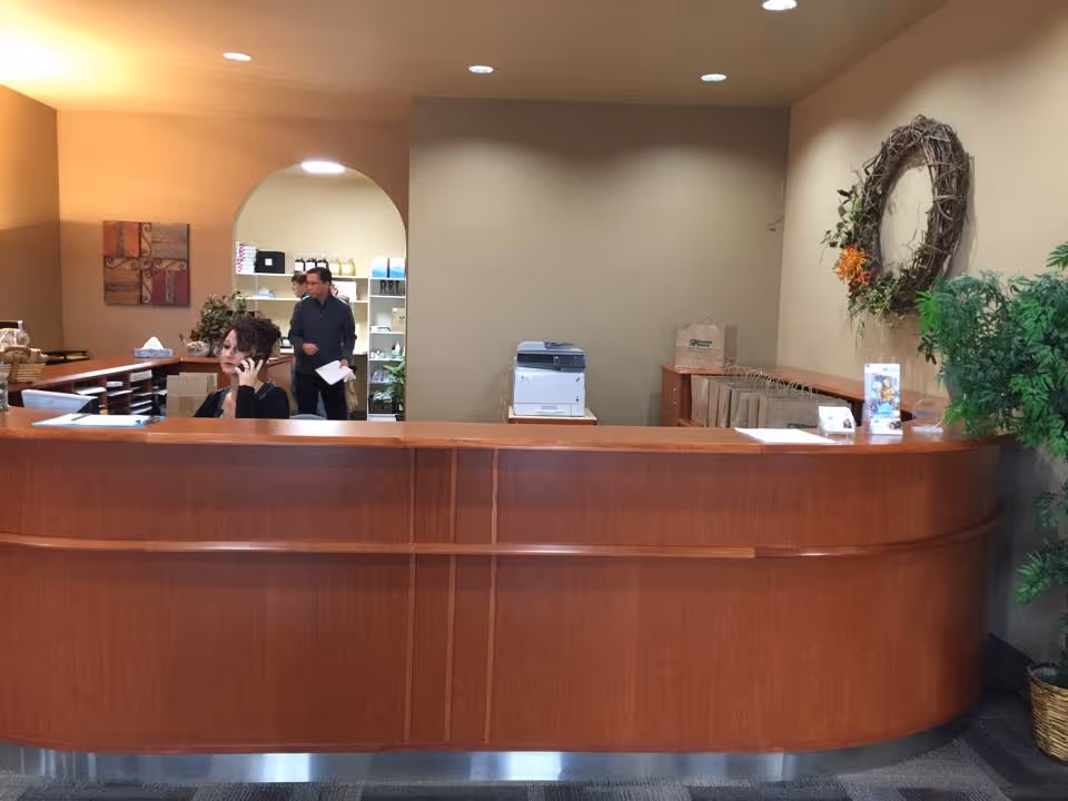 Curved wooden reception desk in a lobby with staff and a printer behind.