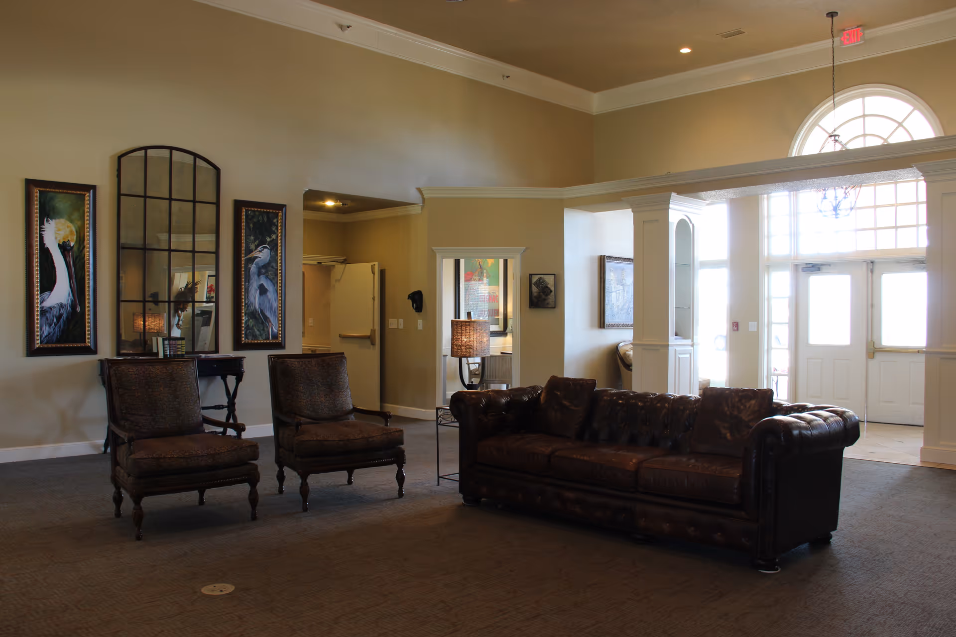 Spacious senior living lobby with brown leather sofa, two chairs, lamps, and arched windows.