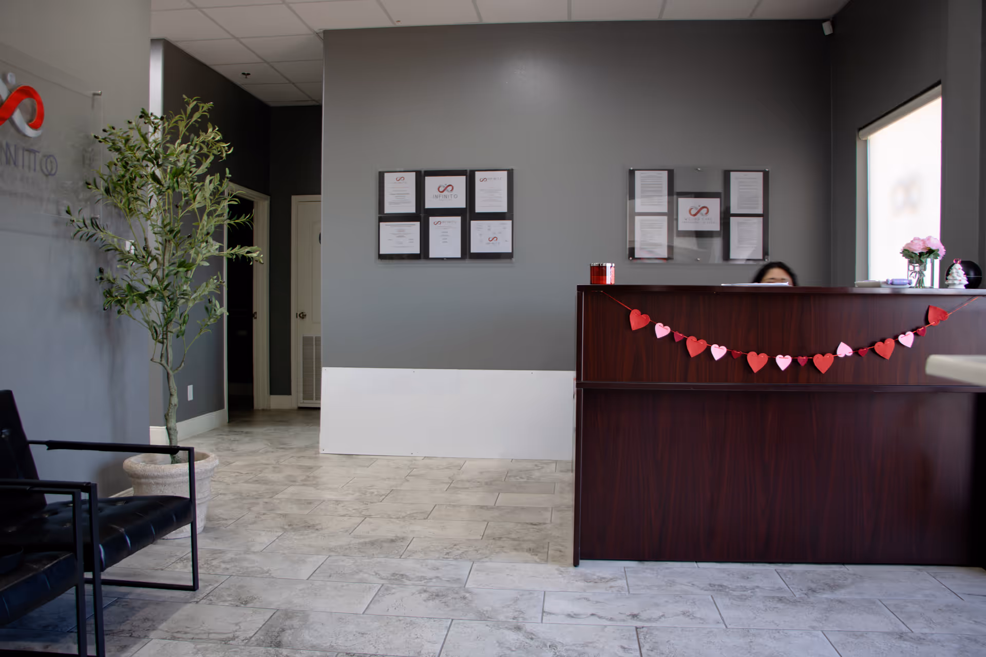 Reception area with a dark desk, heart garland, certificates on wall, plant, and seating.