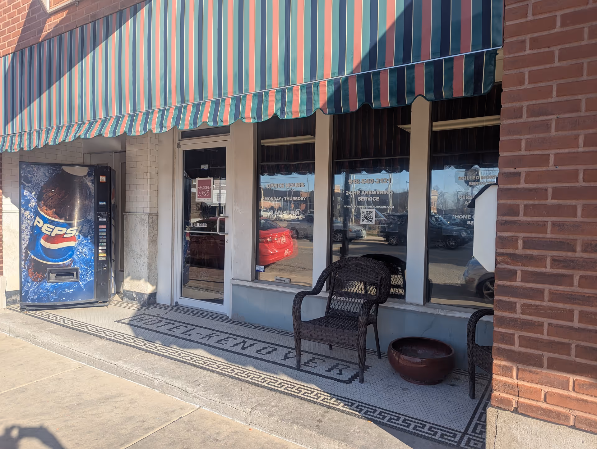 Exterior storefront with striped awning, glass doors, vending machine, and outdoor chairs.