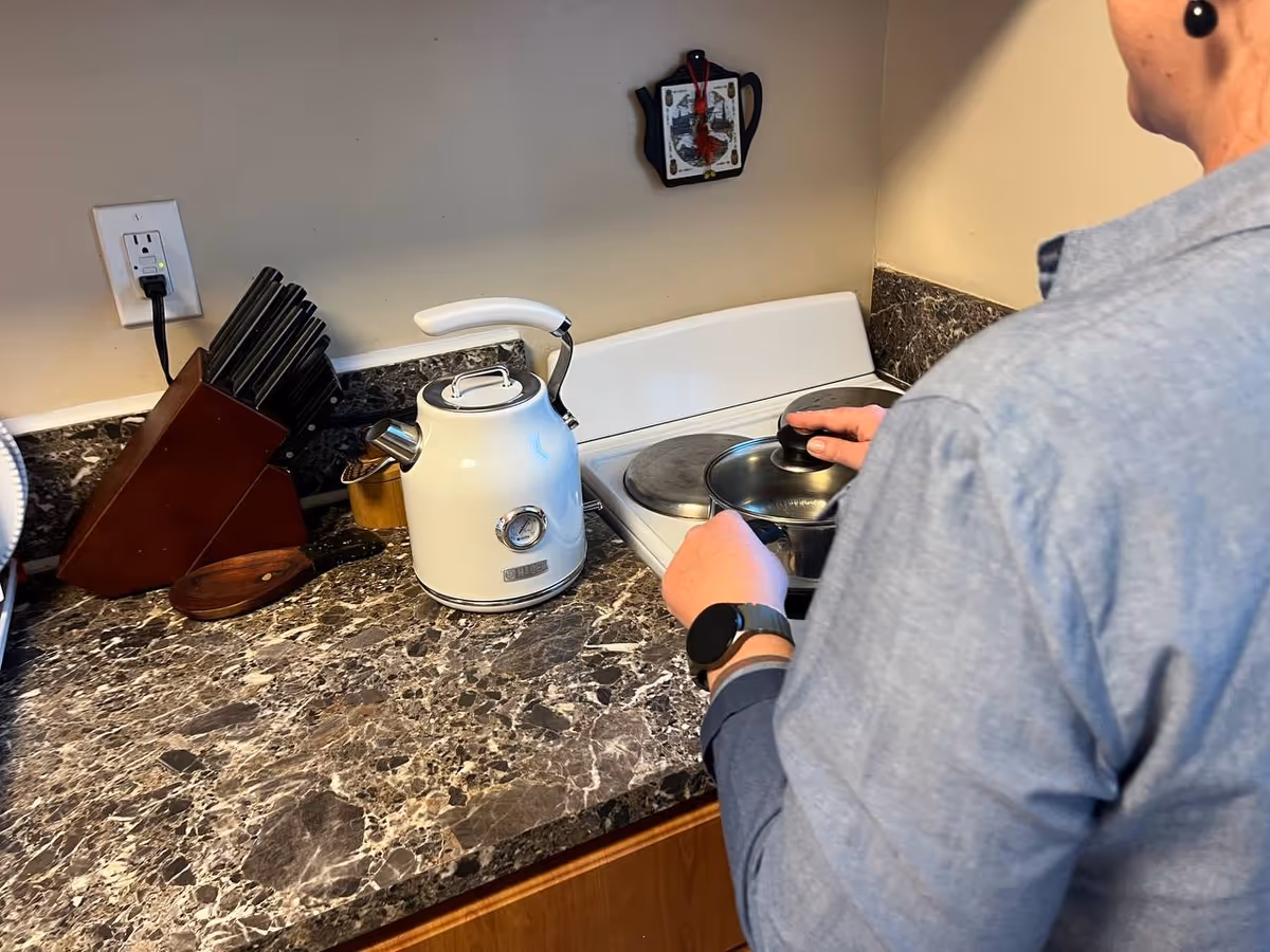 Person in gray shirt cooks on a stove with kettle and kitchen utensils on marble counter