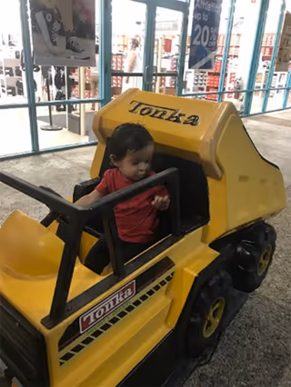 A child sits in a yellow Tonka ride-on toy outside a storefront.
