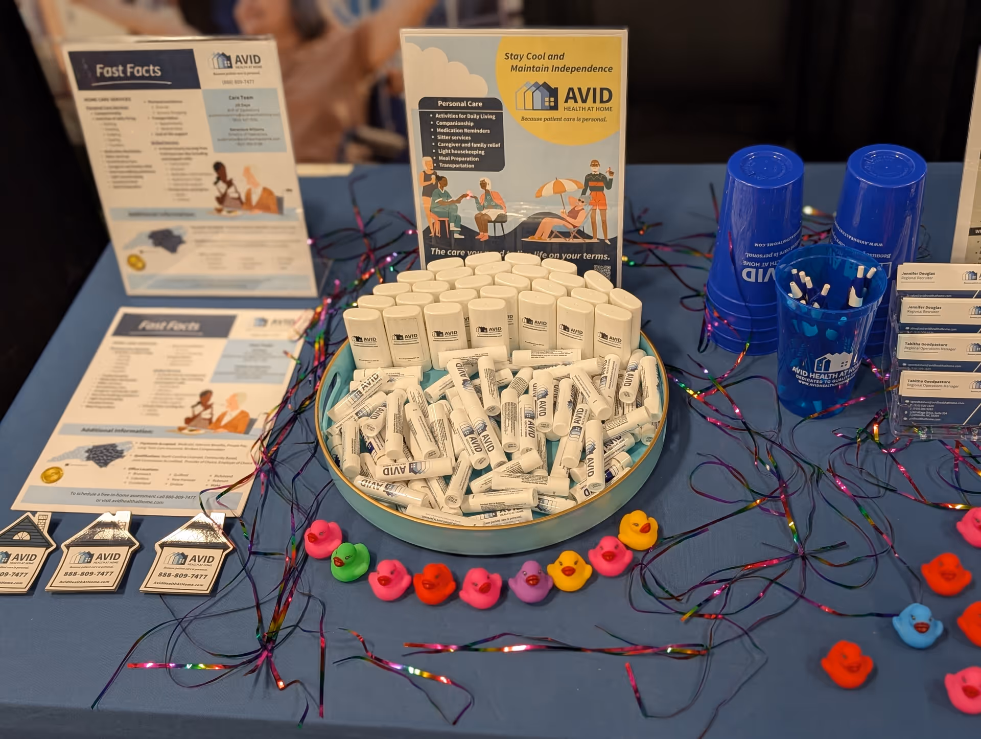 Promotional table with AVID Health at Home brochures, pill bottles, and colorful decorations.