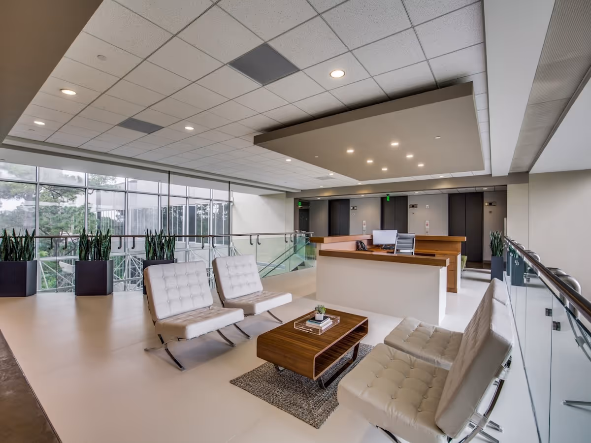 Modern senior living lobby featuring white leather seating, glass railing, a reception desk, and large windows.