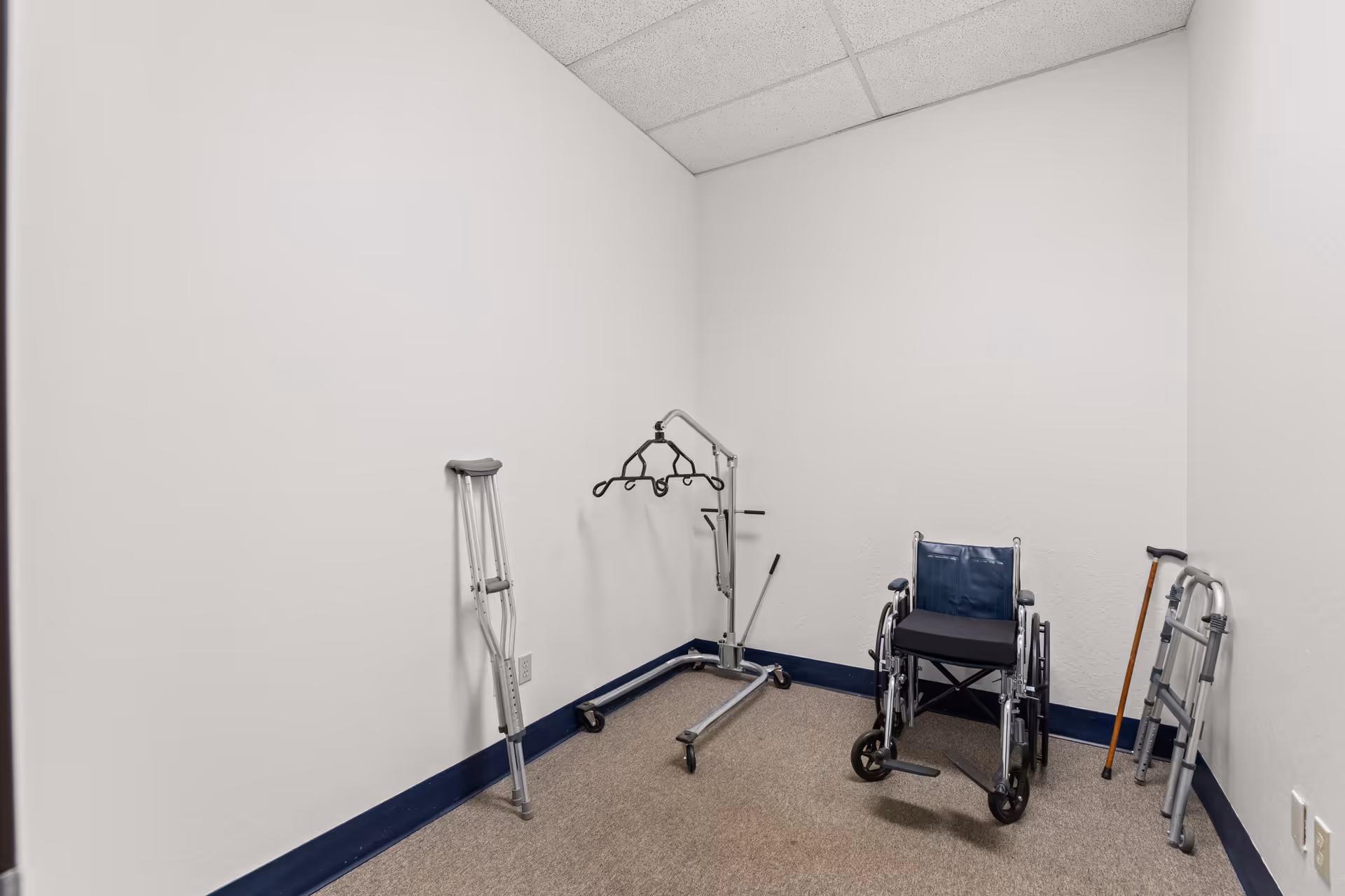 Small empty storage room with a wheelchair, crutches, and a walker against white walls.