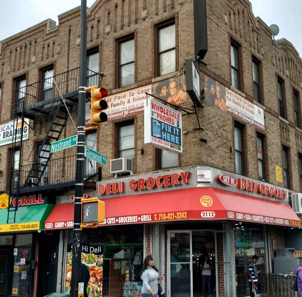 Brick multi-story building with a deli/grocery storefront on a busy city street.