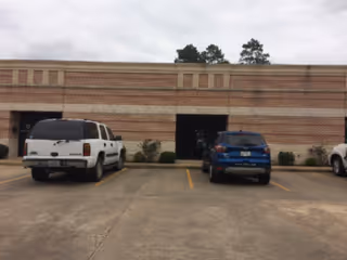 Brick building facade with a parking lot and two parked vehicles in front.