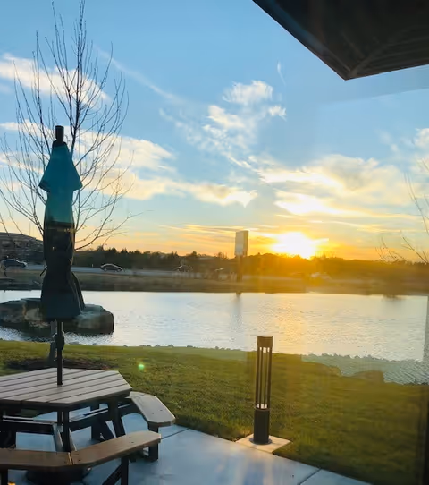 Outdoor patio with a picnic table and umbrella overlooking a lake at sunset.