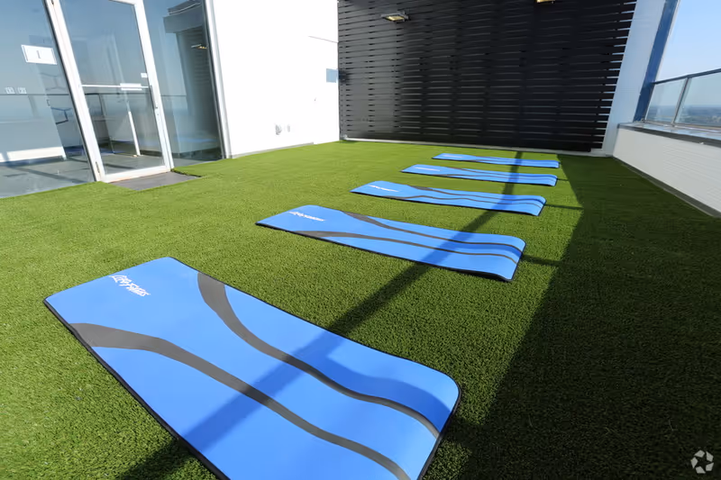 Outdoor balcony with blue exercise mats laid on green artificial turf.