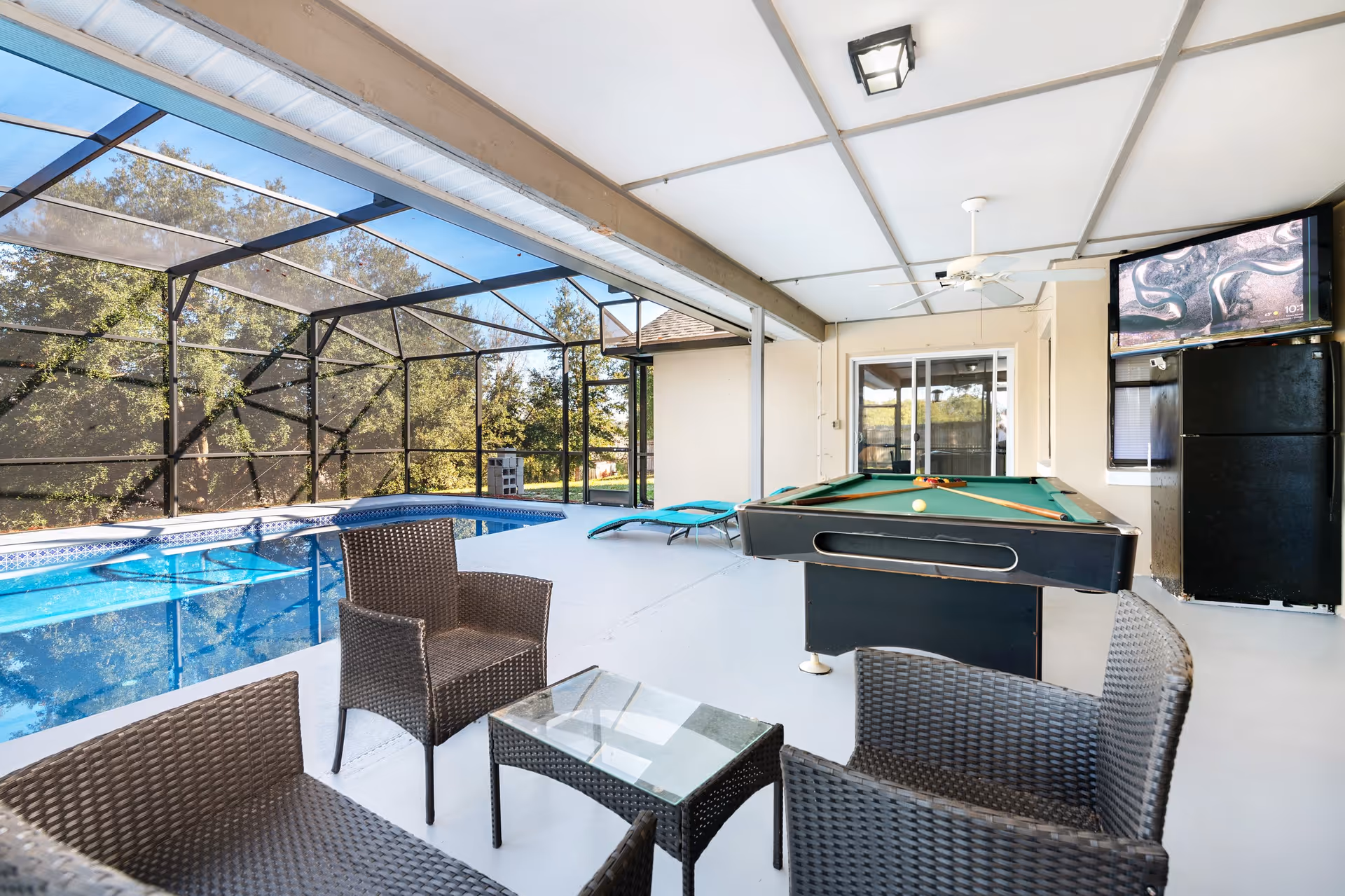 Indoor covered recreation area featuring a pool, pool table, wicker seating, and a fridge.