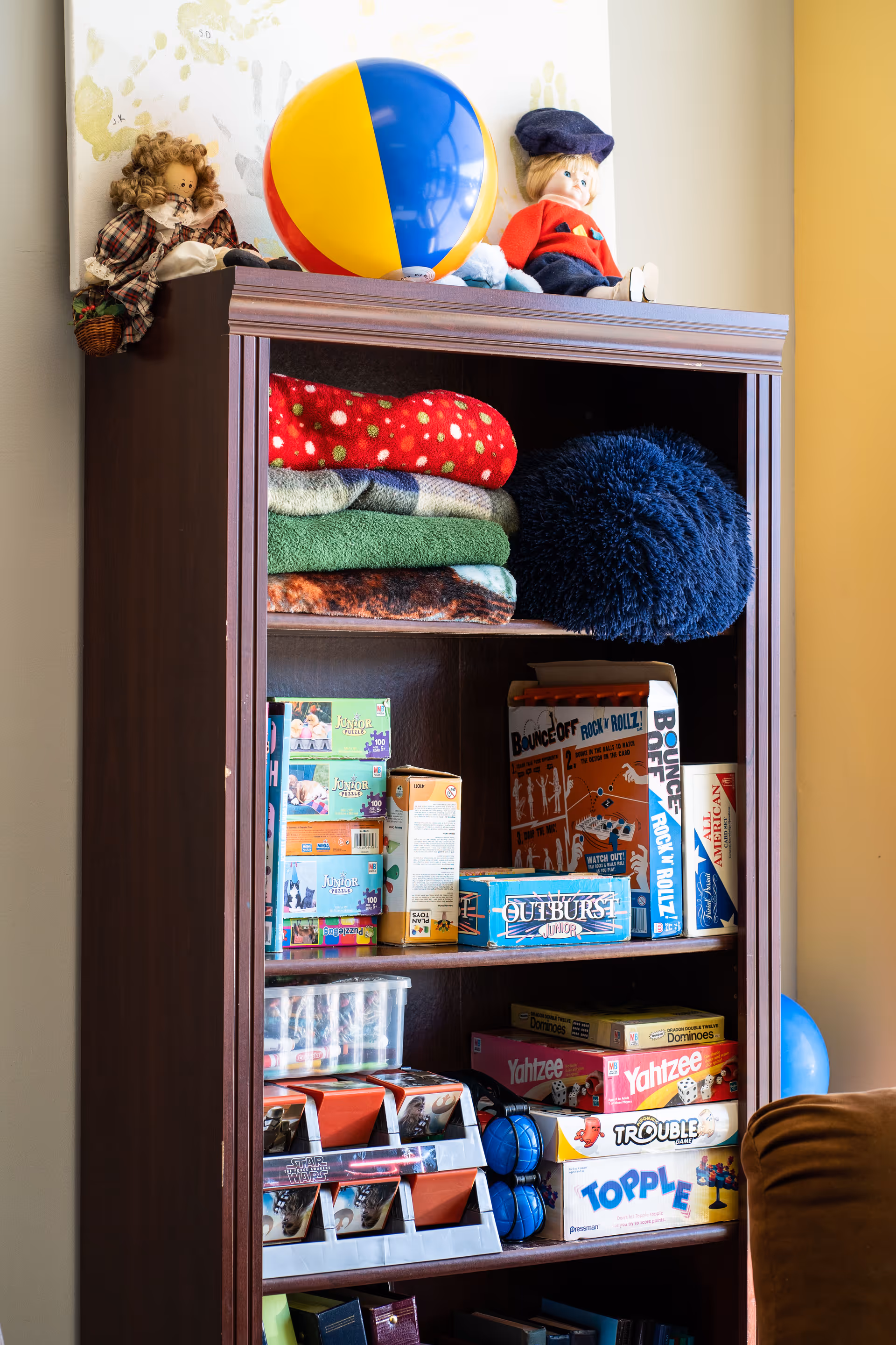 Tall wooden cabinet stocked with blankets, toys, and board games.