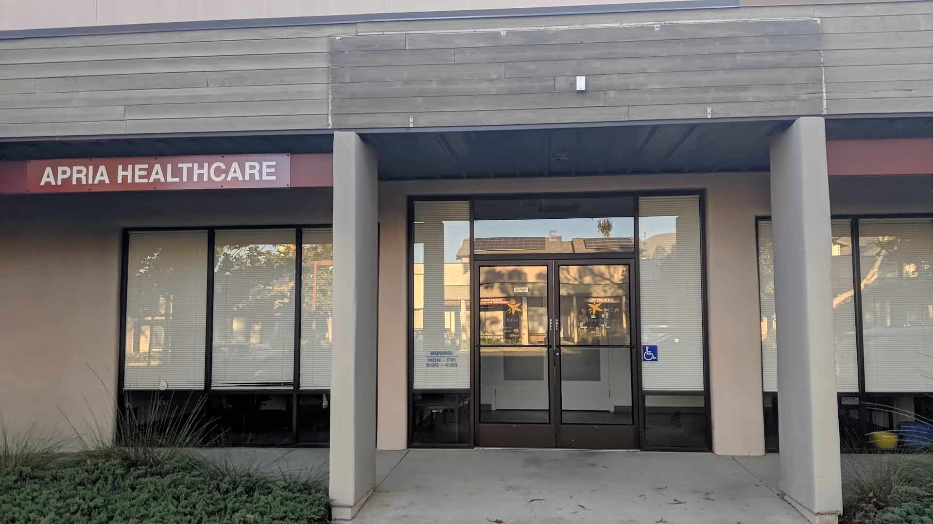 Exterior view of Apria Healthcare building with glass entry doors and a wheelchair sign.