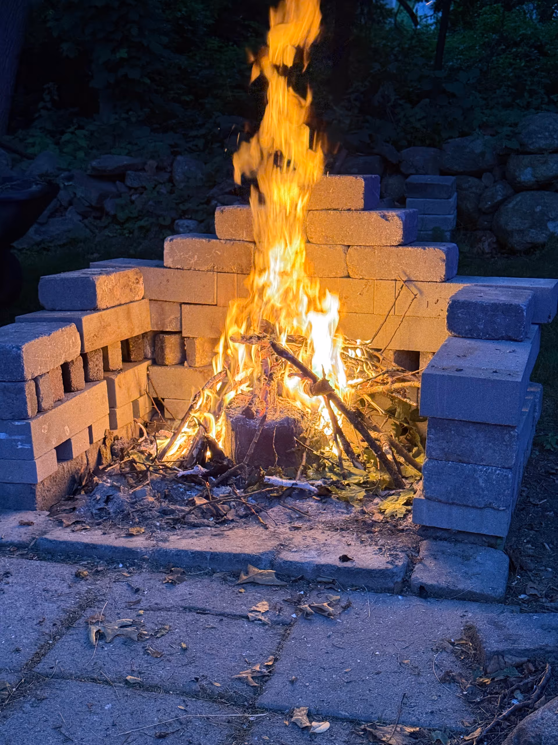 Outdoor fire pit constructed from stacked concrete blocks atop a paved stone patio.