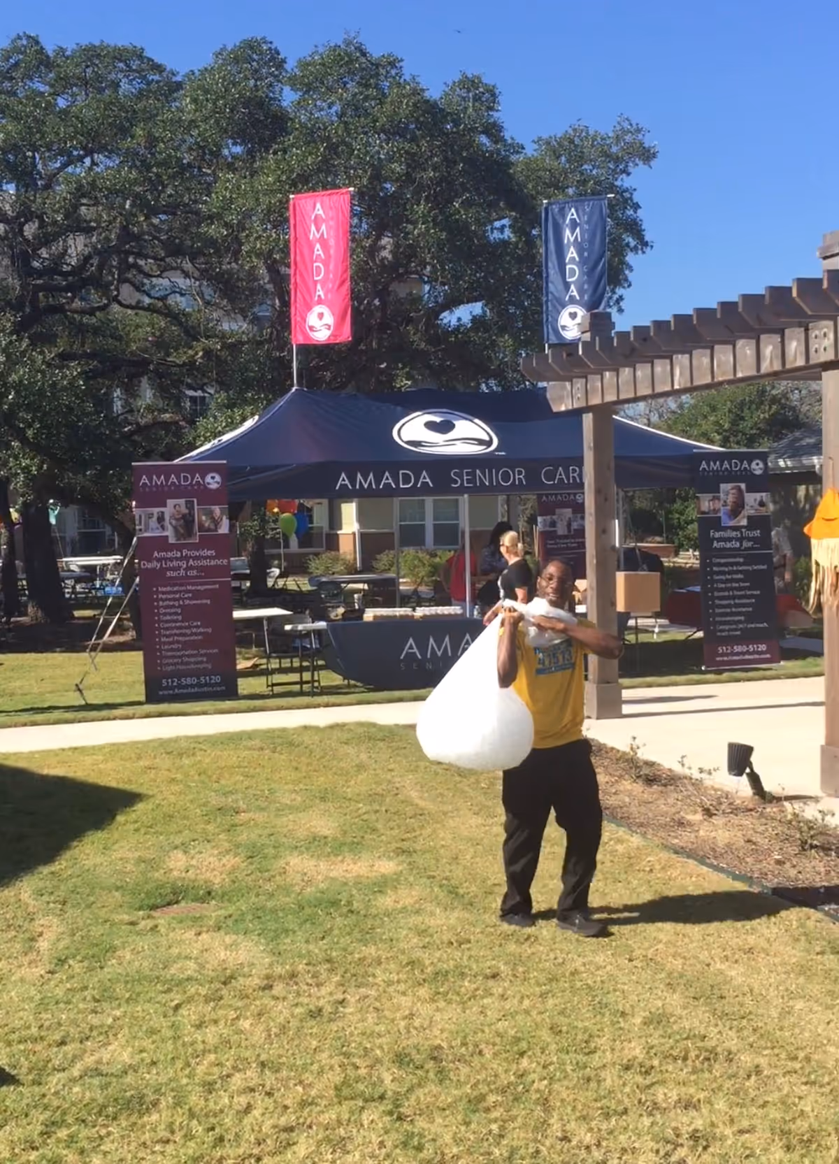 Amada Senior Care outdoor booth with tents, banners, and a man carrying a large white bag.