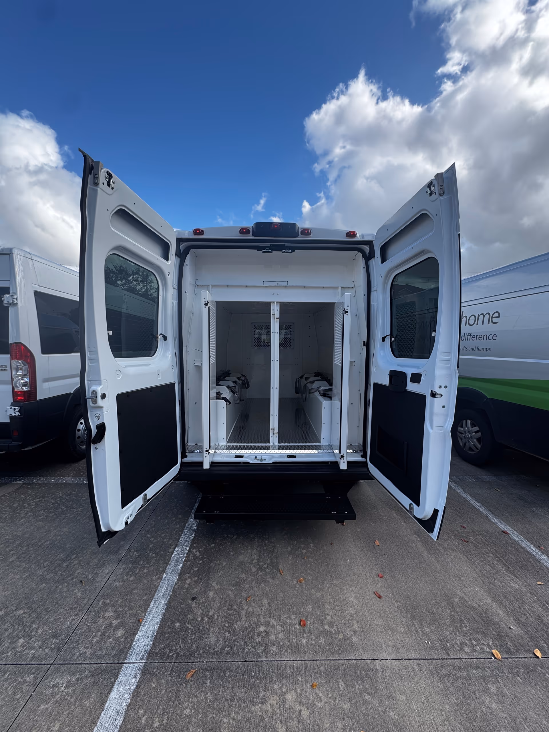 Open rear doors reveal an empty mobility van interior with a central lift frame.