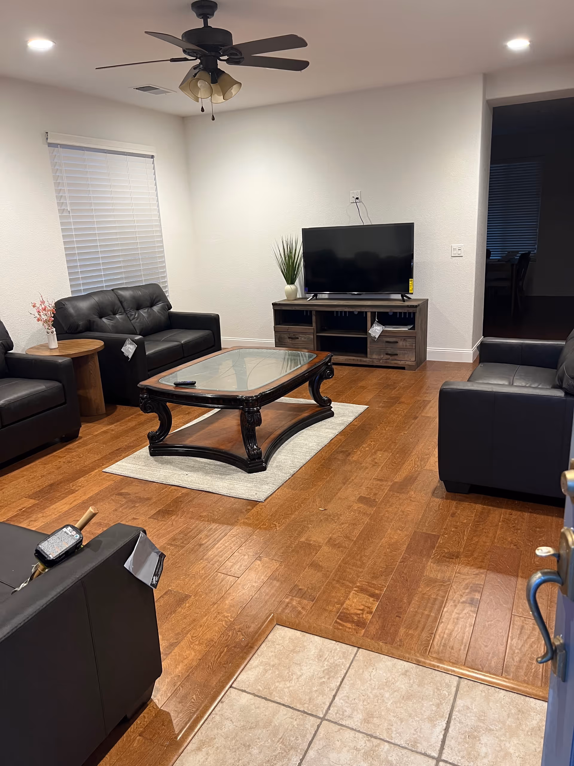 A furnished living room with black leather sofas, a glass coffee table, and a TV.