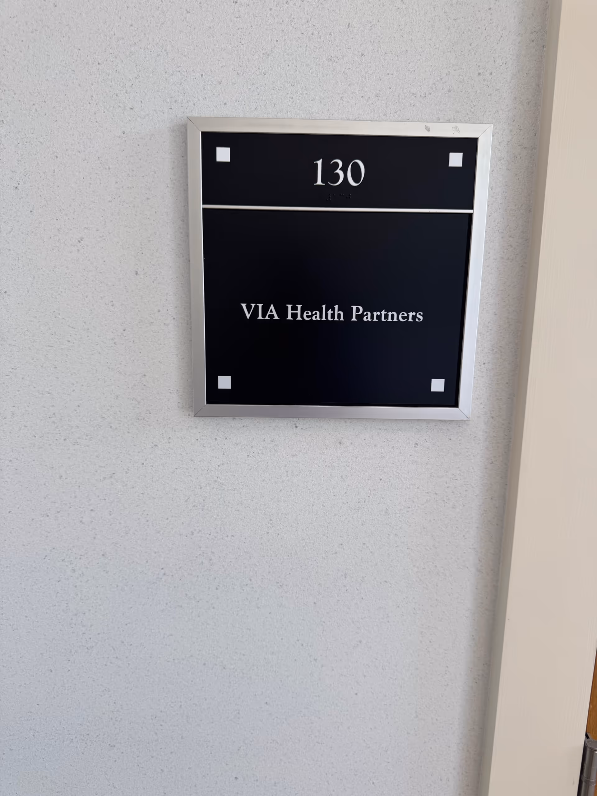 Interior wall sign displaying room 130 for VIA Health Partners.