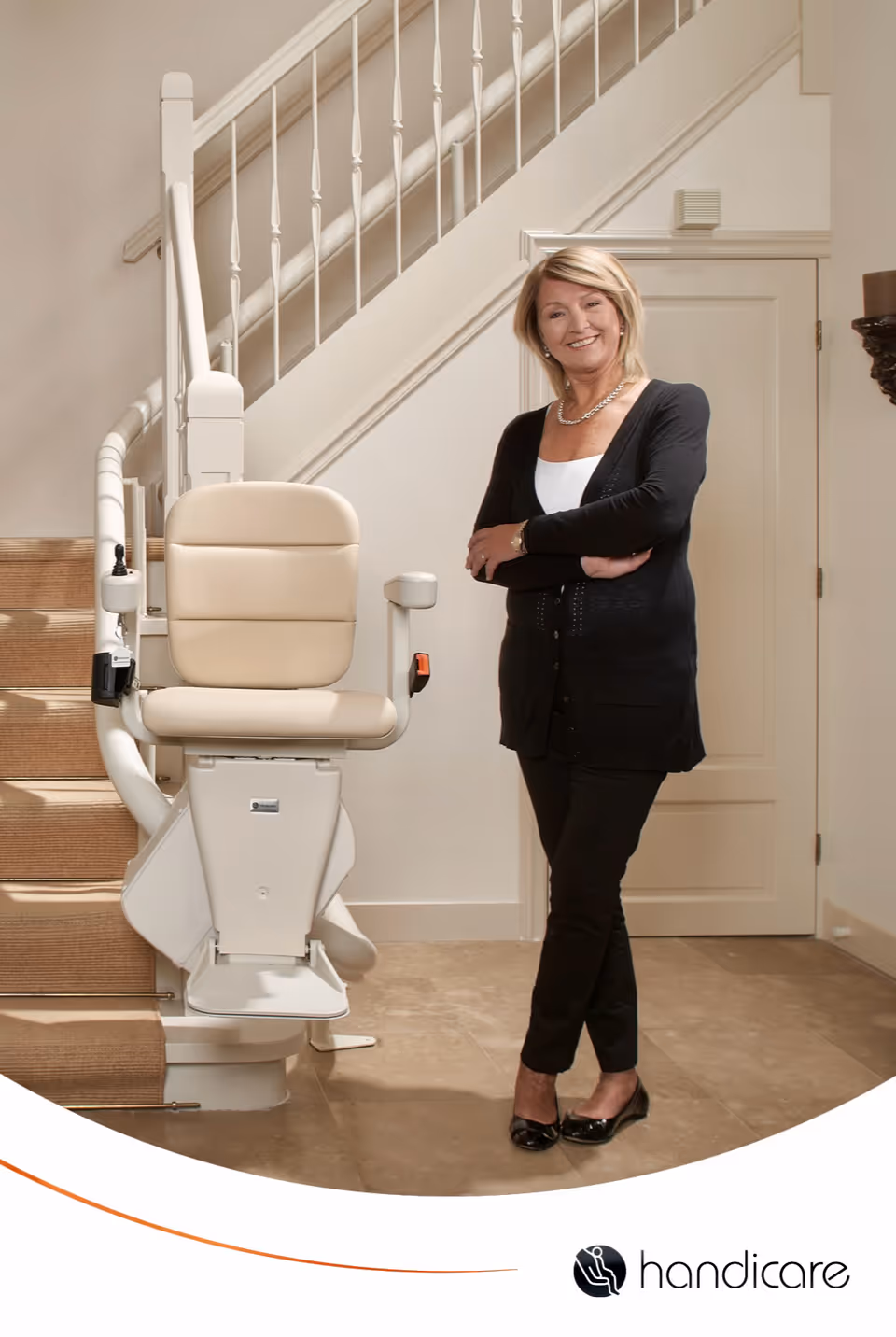 A smiling woman stands beside a stairlift chair inside a light interior near a staircase.