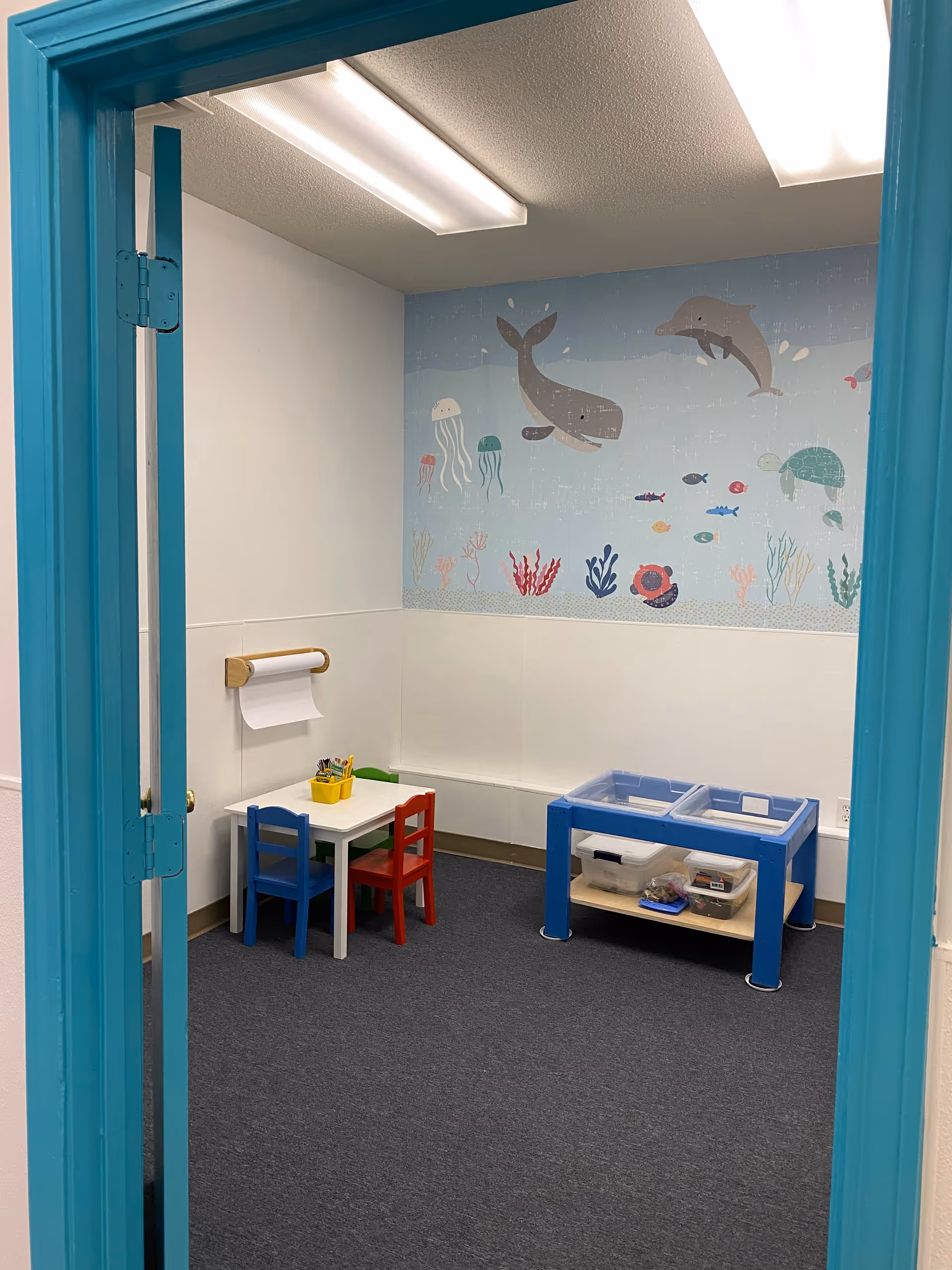 Interior children's activity room with a small table, chairs, and marine mural.