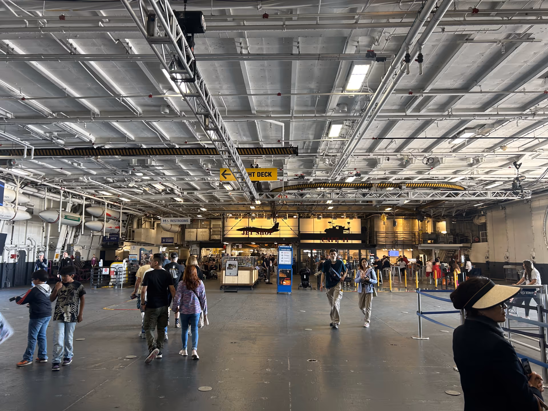 Inside a large industrial-style terminal with travelers walking past overhead signage and equipment.