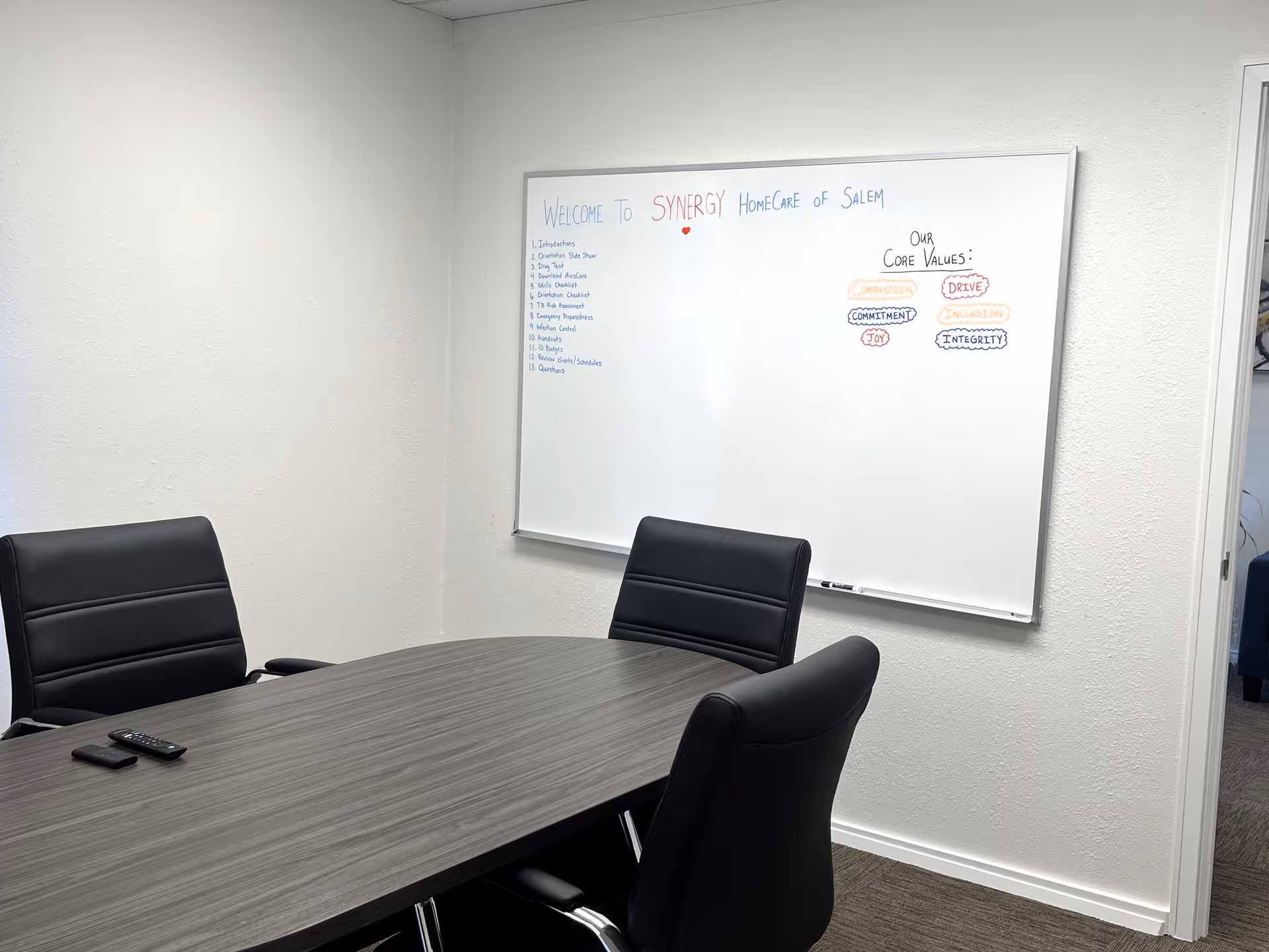 Conference room with table, black chairs, and a whiteboard showing Synergy HomeCare Salem core values.