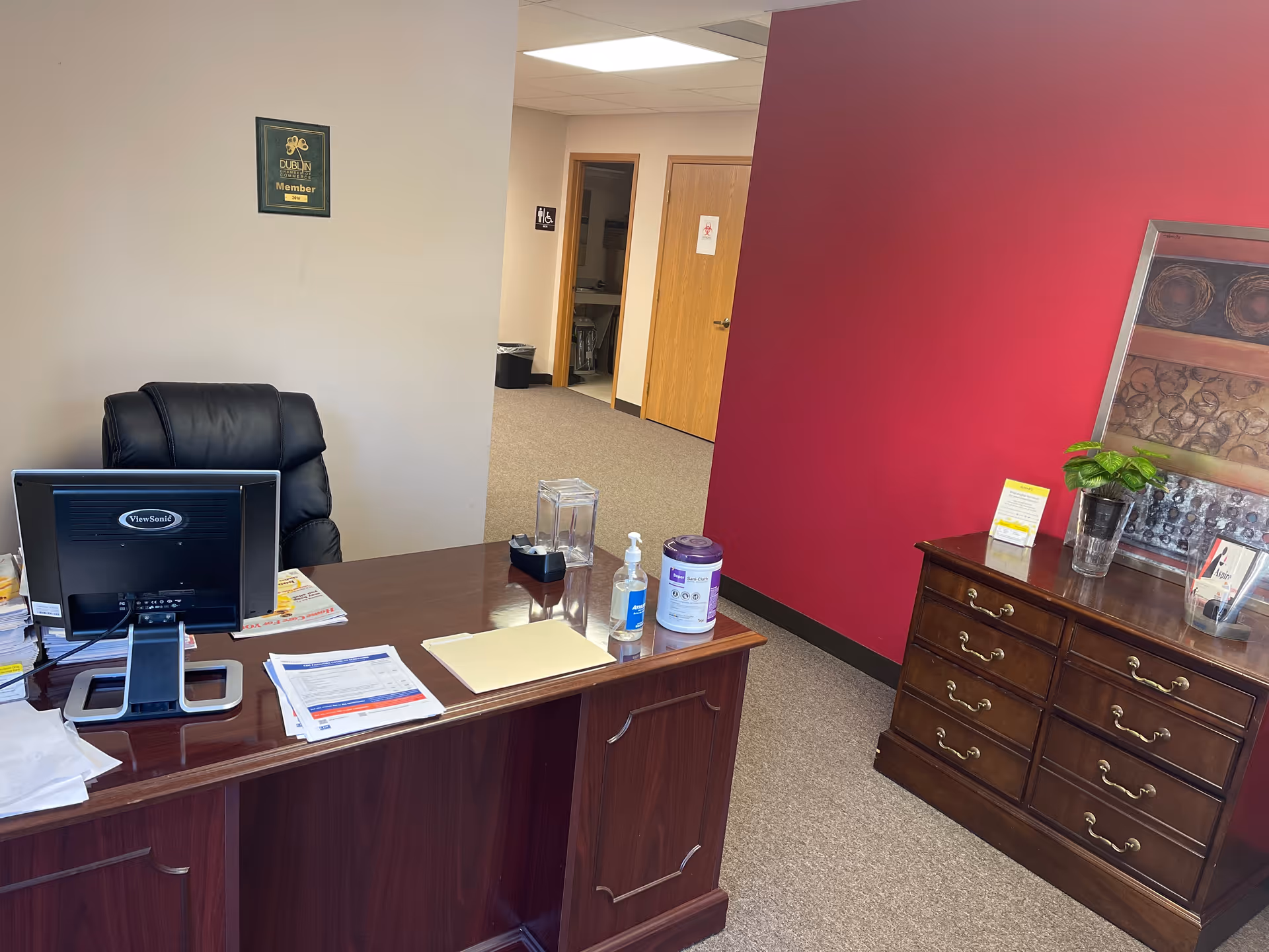 Office reception area with a dark wood desk, computer, and burgundy wall.