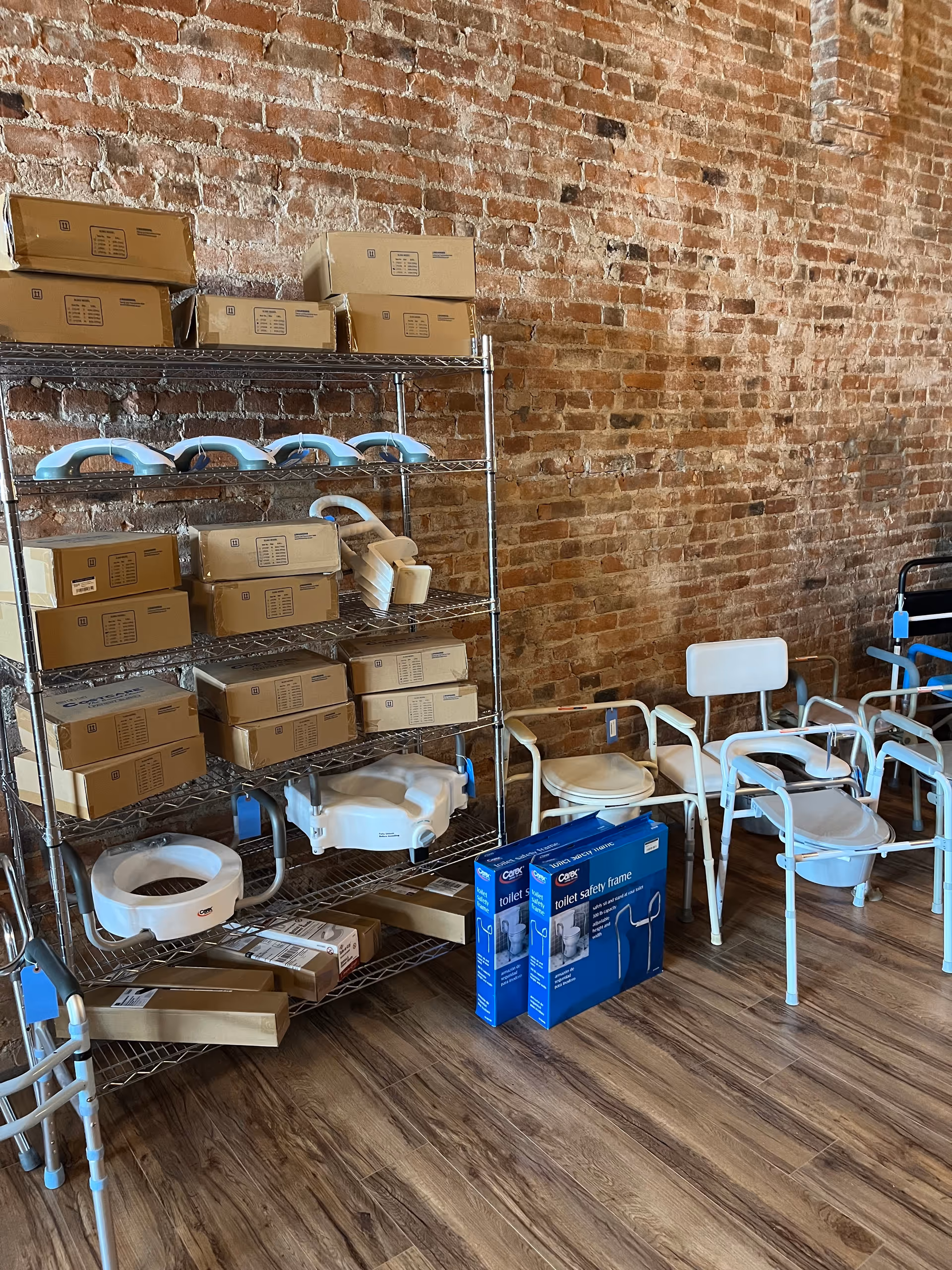 Industrial storage area with metal shelves, cardboard boxes, and white chairs against a brick wall.