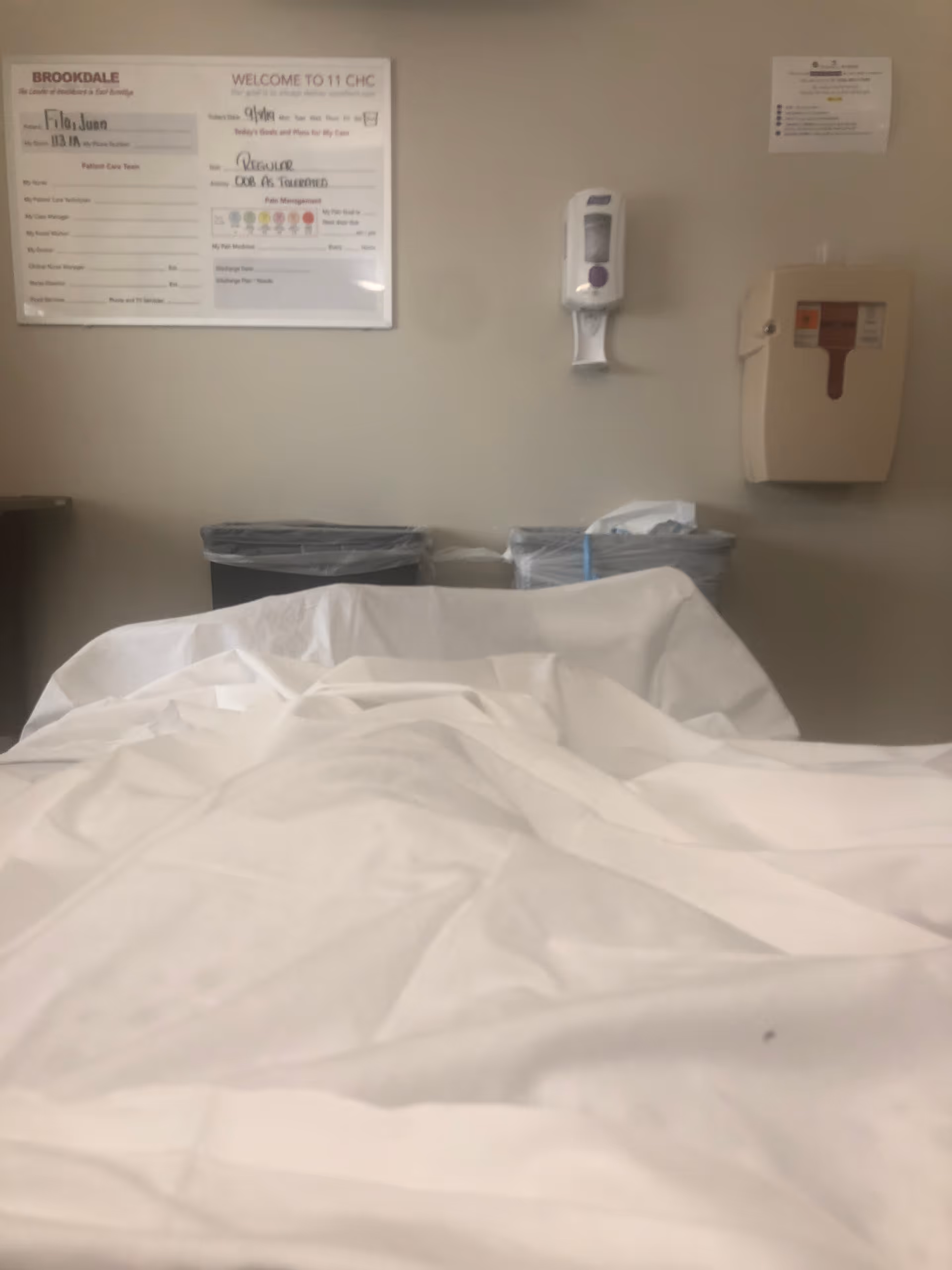 Hospital room with bed, white sheets, and wall-mounted medical equipment.