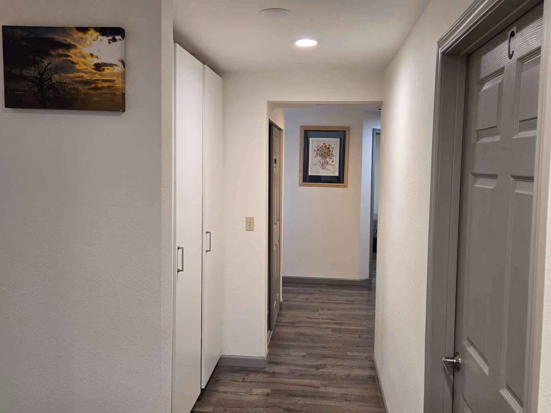 A narrow hallway in a senior care facility with white walls, cabinets, and framed art.