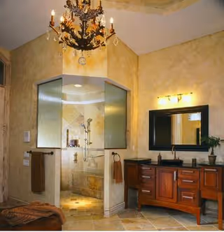 Luxurious bathroom with glass shower, chandelier, and wooden vanity in warm tones.