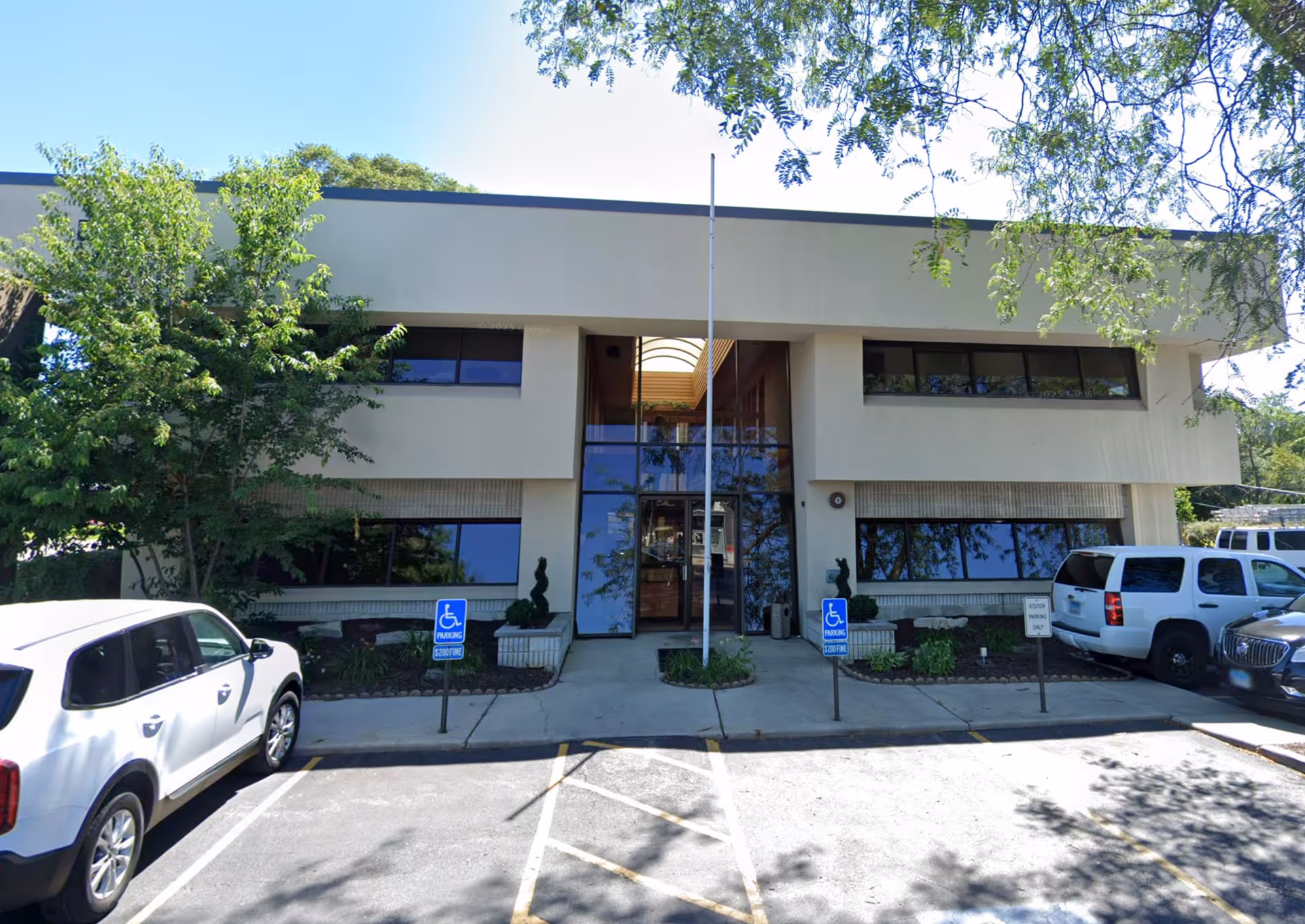 Front view of a beige two-story facility with glass entrance and parked cars.