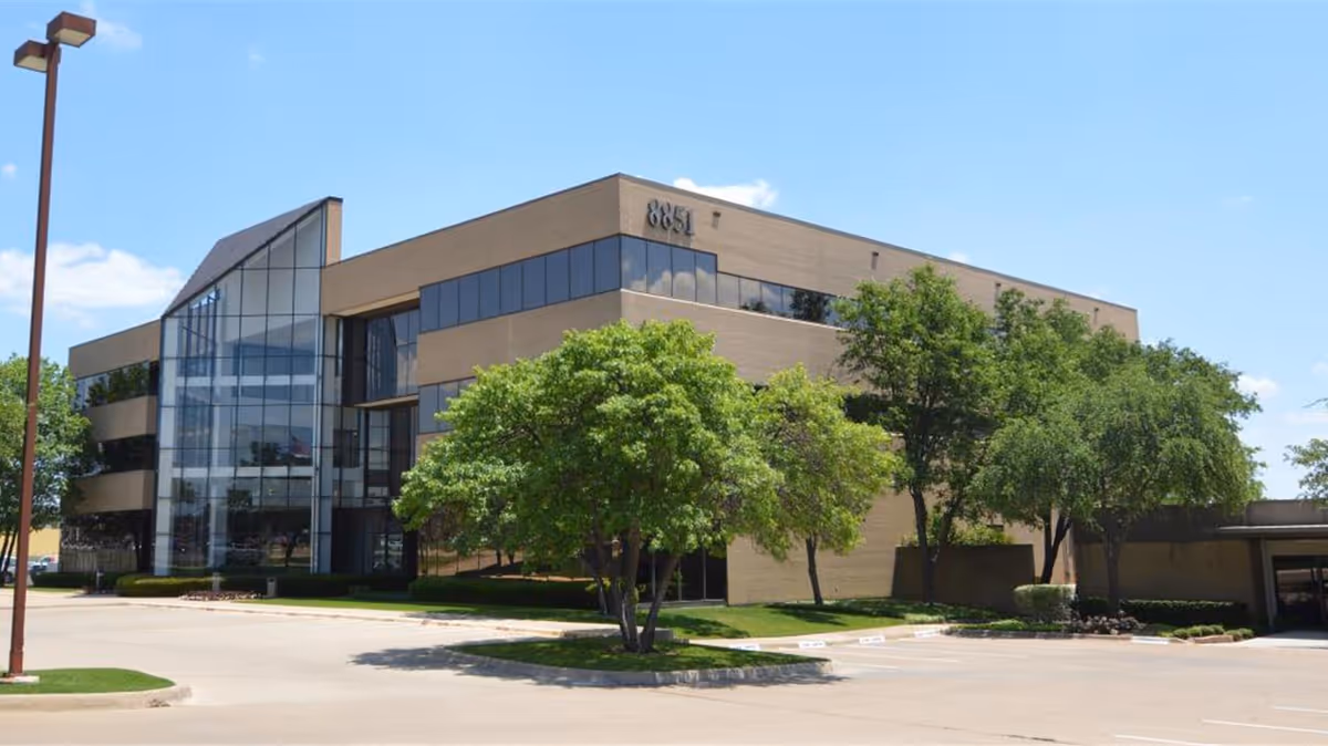 Exterior view of a modern senior living facility with glass entrance and surrounding trees