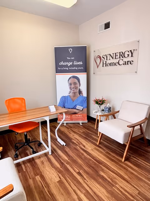 Reception area with a wooden floor, desk, orange chair, banner, and a SYNERGY HomeCare sign.