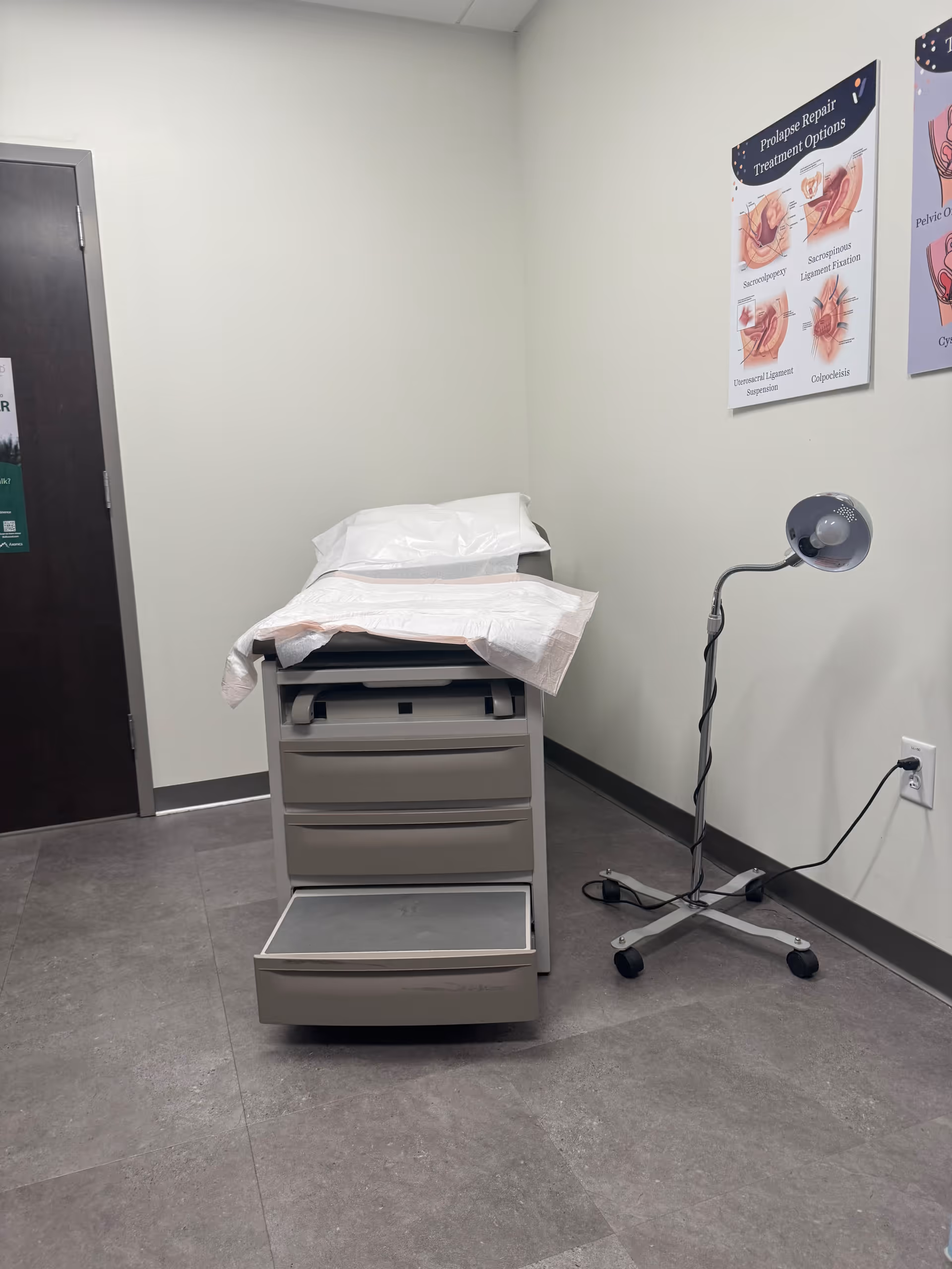 A medical clinic room with a large printer, a floor lamp, and posters on walls.