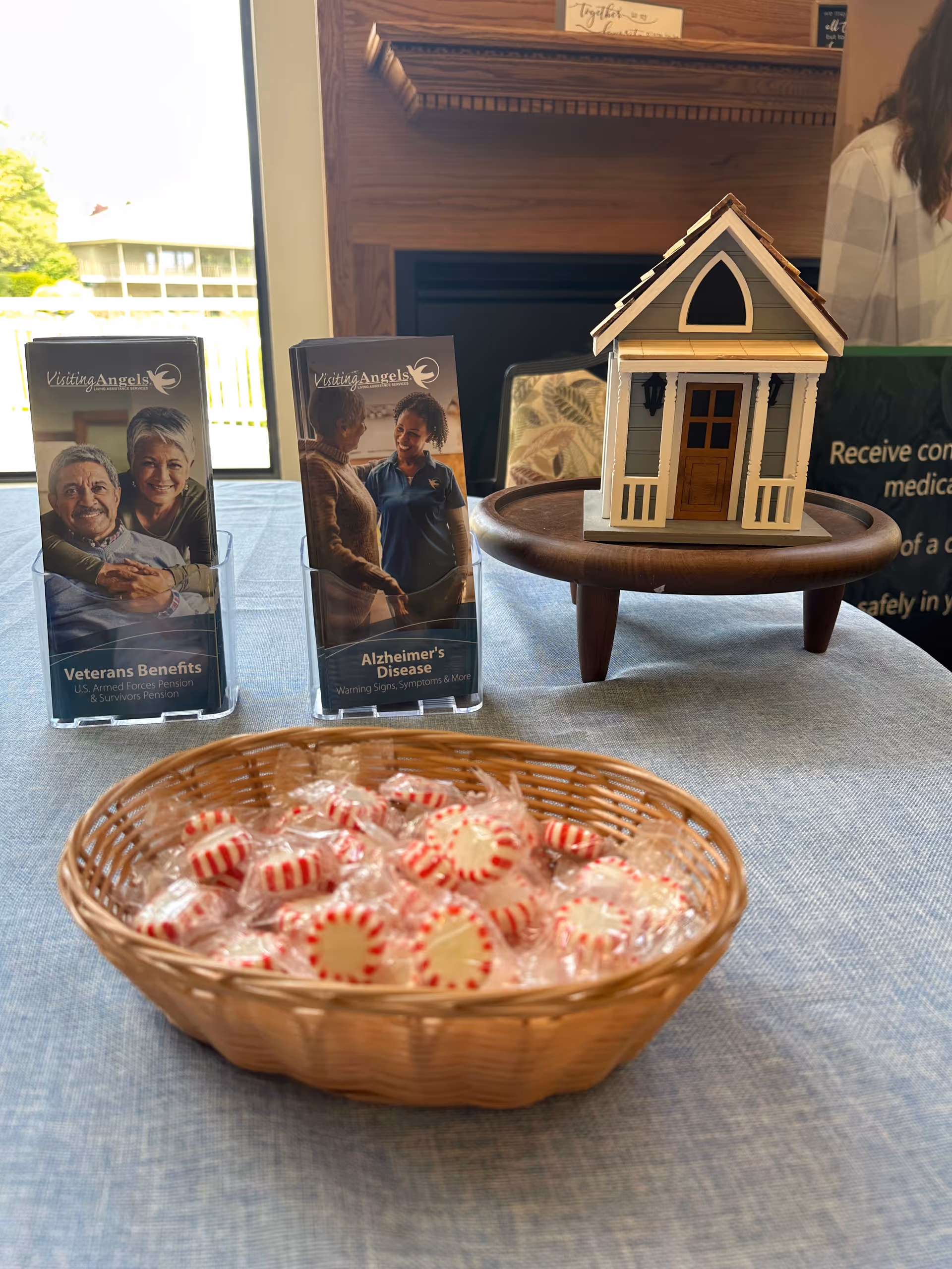 Table display with brochures, a small model house, and a candy basket at Visiting Angels.