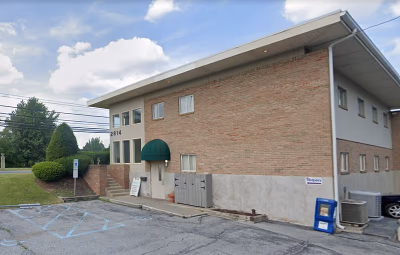 Two-story brick senior living facility with green awning entrance and parking lot.