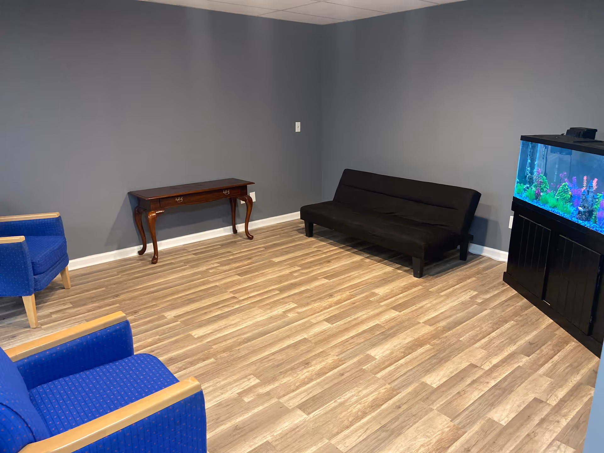 A small lounge area with blue chairs, a black sofa, and an aquarium.