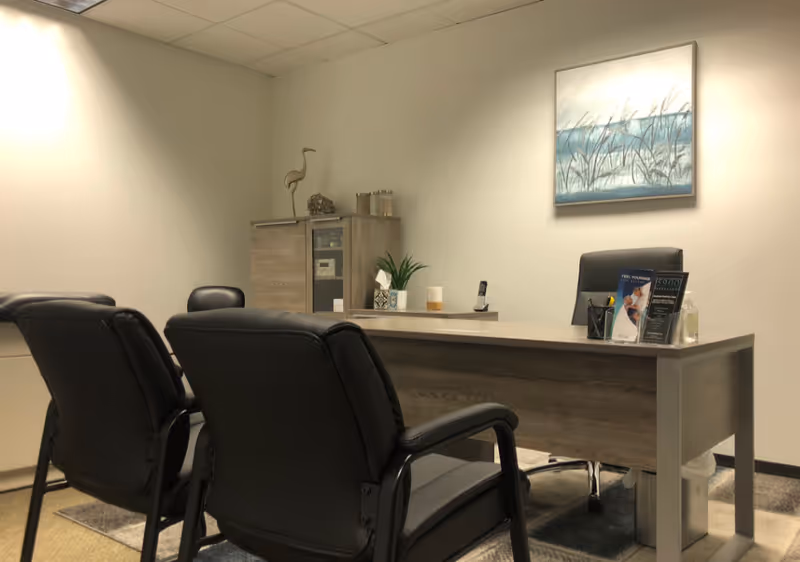 Reception desk with black chairs, artwork, and plants in a neutral facility lobby.