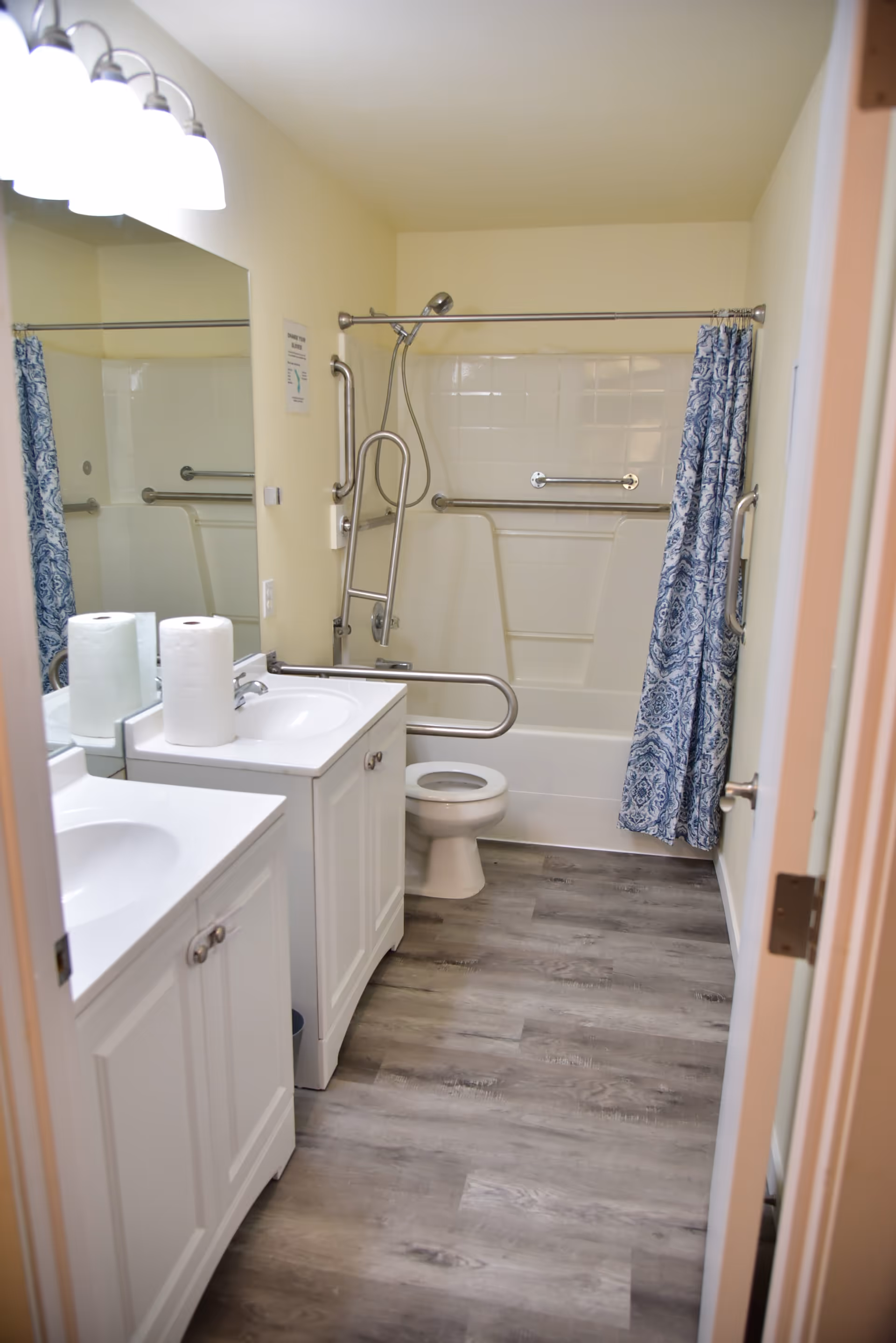 Accessible bathroom with double sinks, mirror, toilet, and a shower with grab bars.