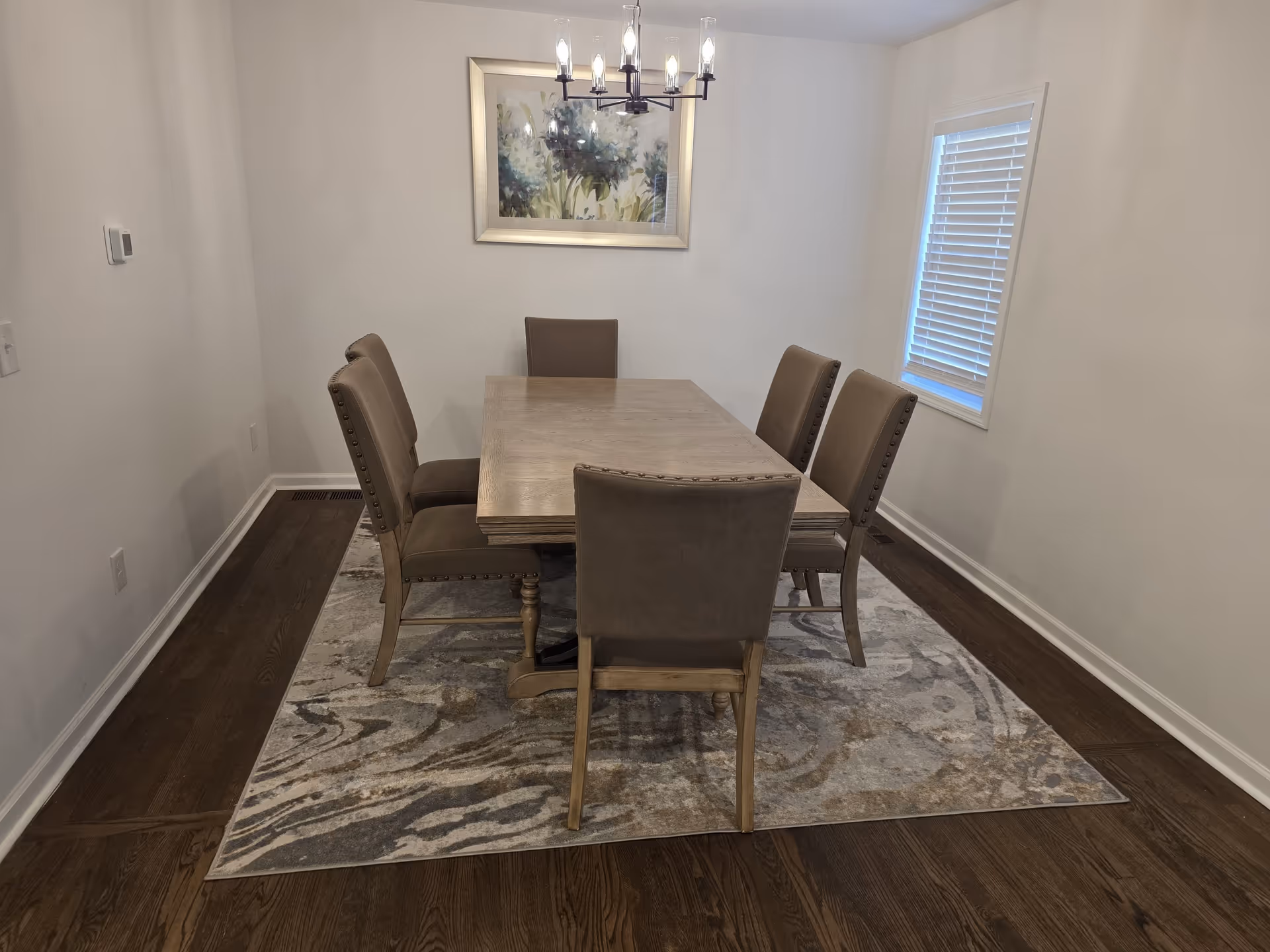 Bright dining room with wood table, six upholstered chairs, rug, and chandelier.