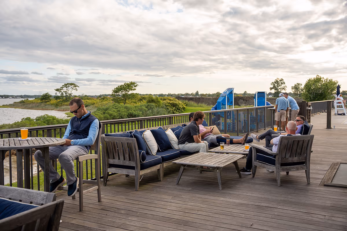 Outdoor wooden deck with seating and people relaxing by the water.