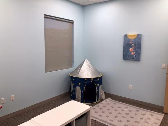 Small therapy room with light blue walls, window shade, and a starry tent on rug.