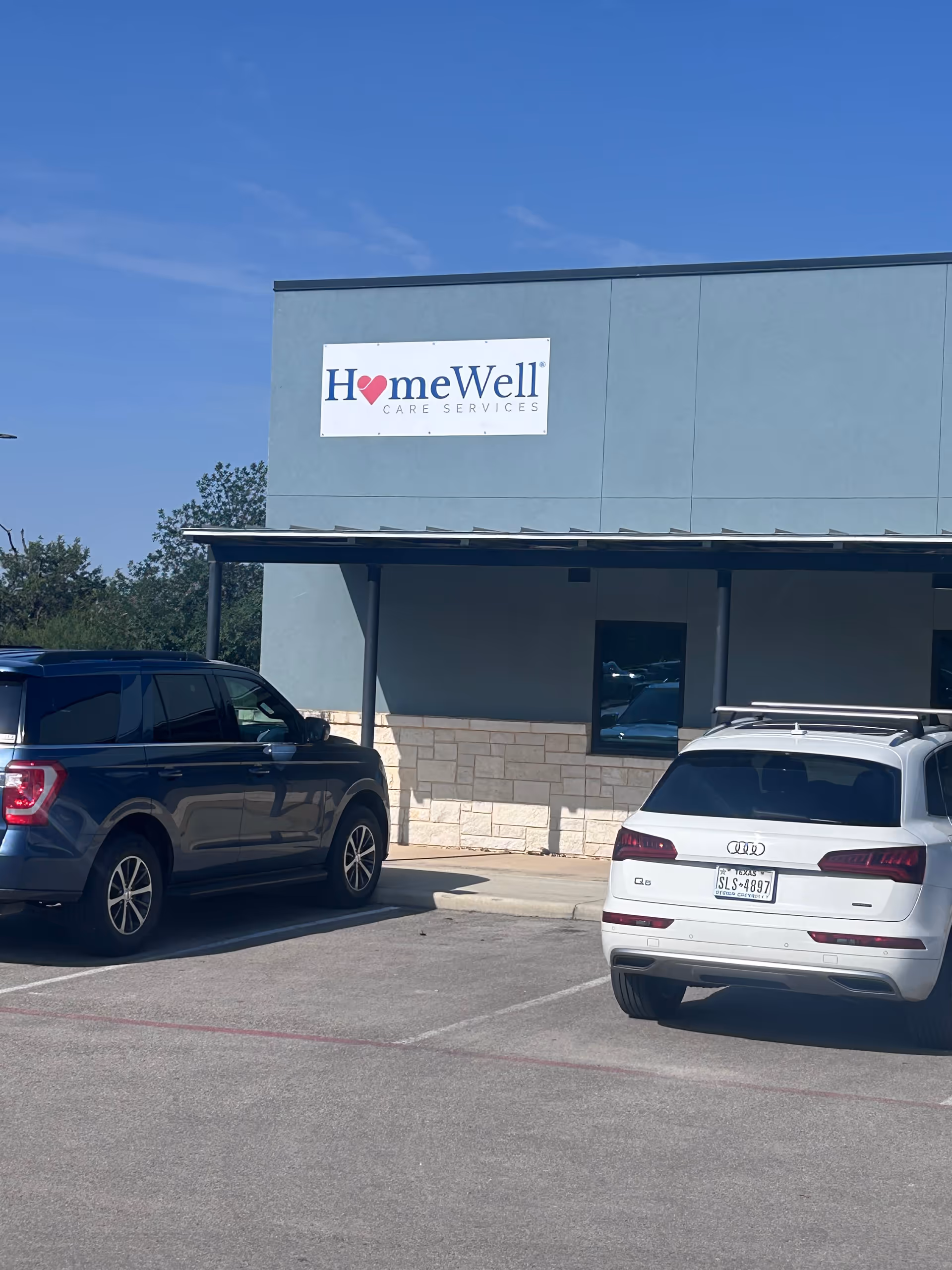 Front view of a HomeWell Care Services building with a parking lot and cars.