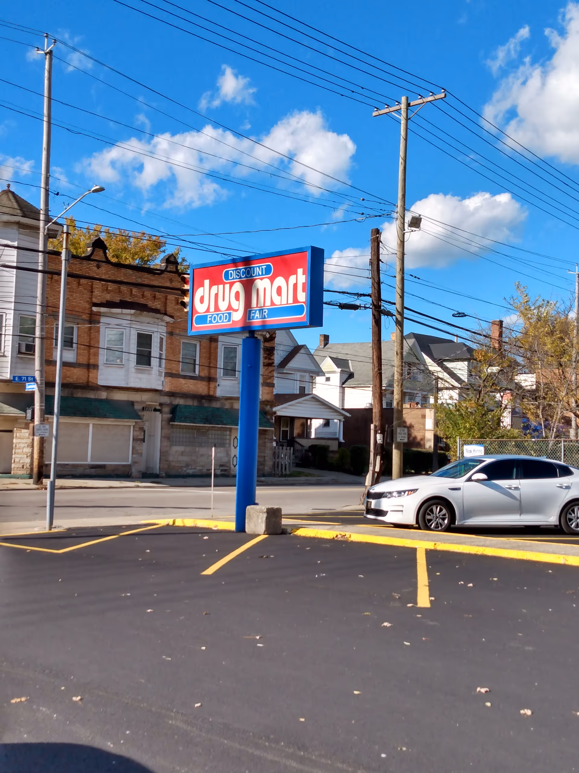 Exterior view of a Discount Drug Mart storefront with a blue pole sign and parked car.
