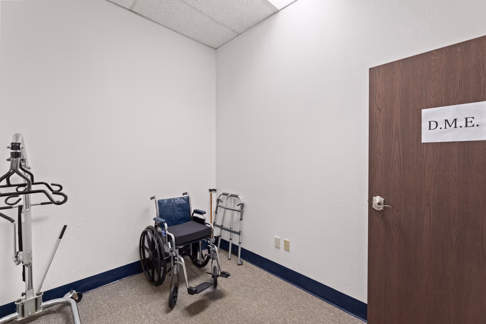 A narrow interior utility room with wheelchair, walker, and medical equipment against white walls.